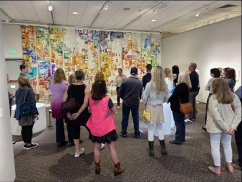 Group of visitors looks at plastic art on wall with artist facing them
