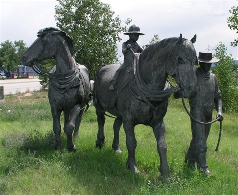Bronze sculpture of man and boy leading three horses