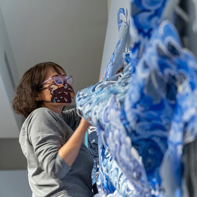Image of a female artist hanging blue scalloped artwork on a wall