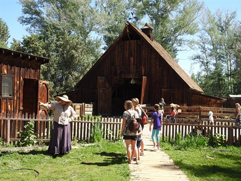 women in pioneer clothing pointing out items in garden area to visitors